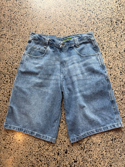 Wrangler mid blue wash denim jorts, size 30W, laid on polished concrete background. Knee cut with classic stitching and soft wash
