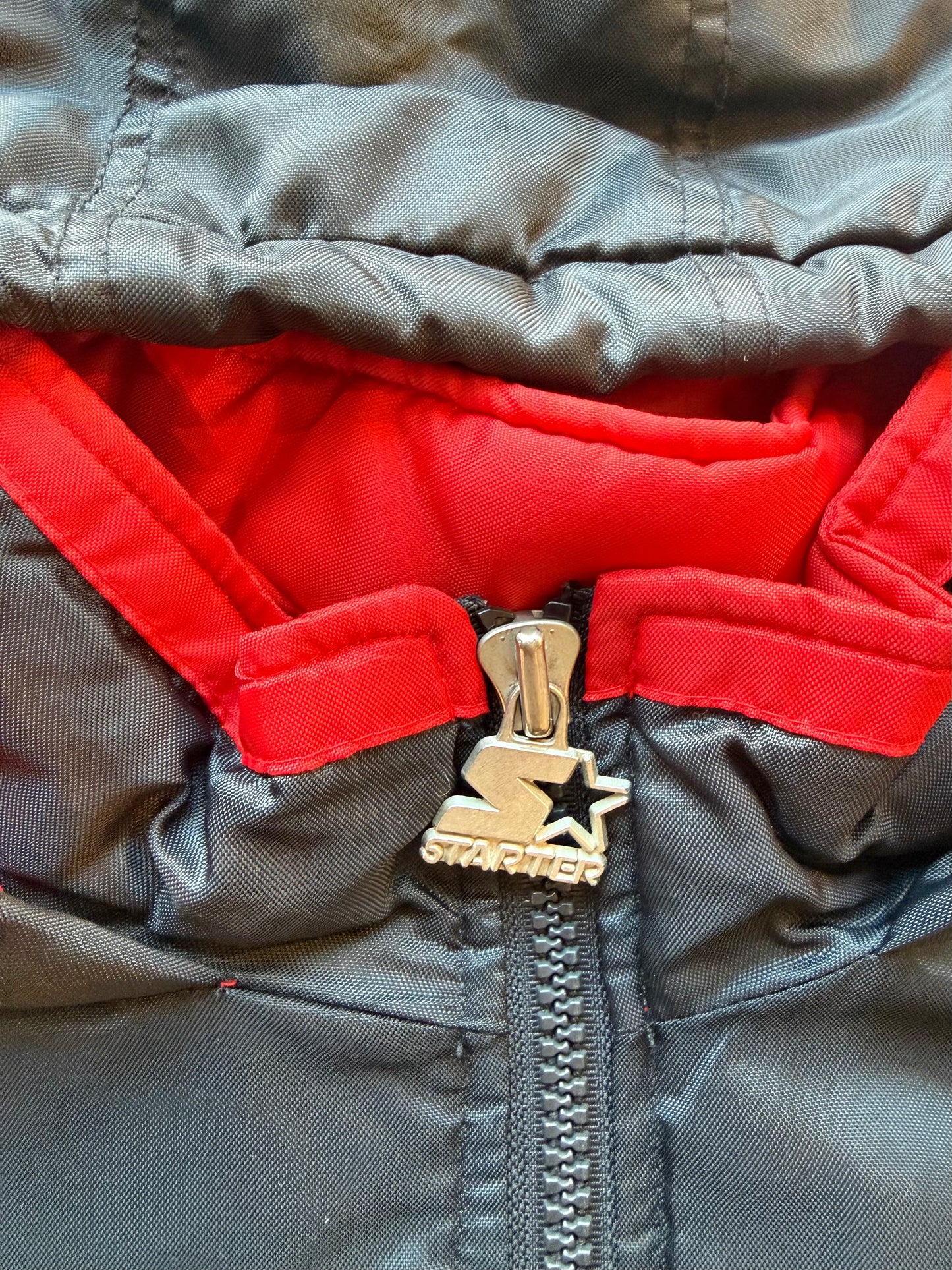 90s black and red Starter jacket size M laid flat on polished concrete background, vintage jacket with bold colour blocking and classic Starter fit.