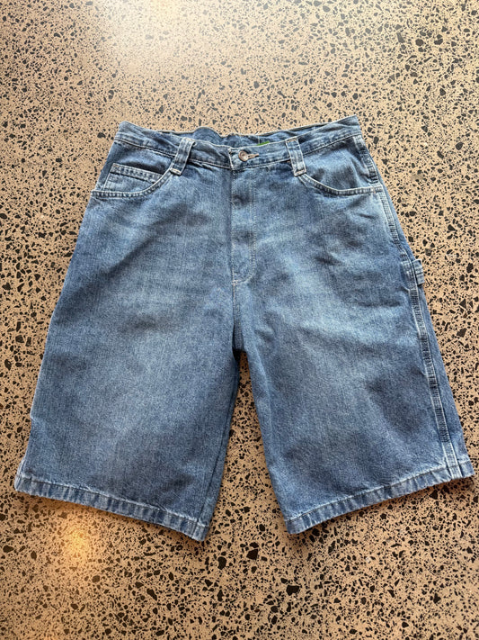 Wrangler  mid blue wash denim jorts, size 30W, laid on polished concrete background. Knee cut with classic stitching and soft wash