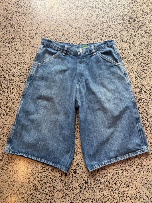 Wrangler Original dark blue wash denim jorts, size 30W, laid on polished concrete background. Knee cut with classic stitching and soft wash
