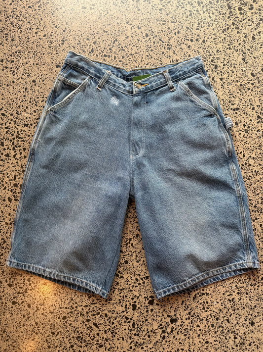 Blue mid-wash denim jorts, size 30W, laid on polished concrete background. Knee cut with classic stitching and soft wash