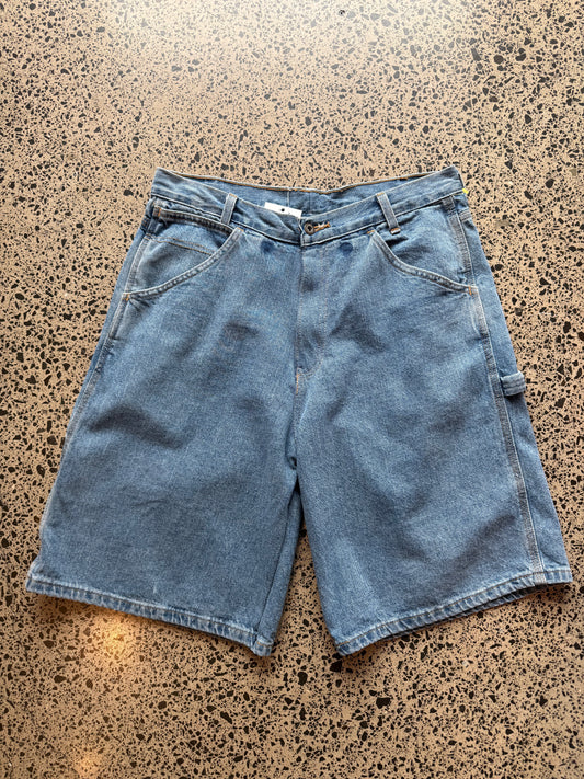 Light - mid blue wash denim jorts, size 32W, laid on polished concrete background. Knee cut with classic stitching and soft wash