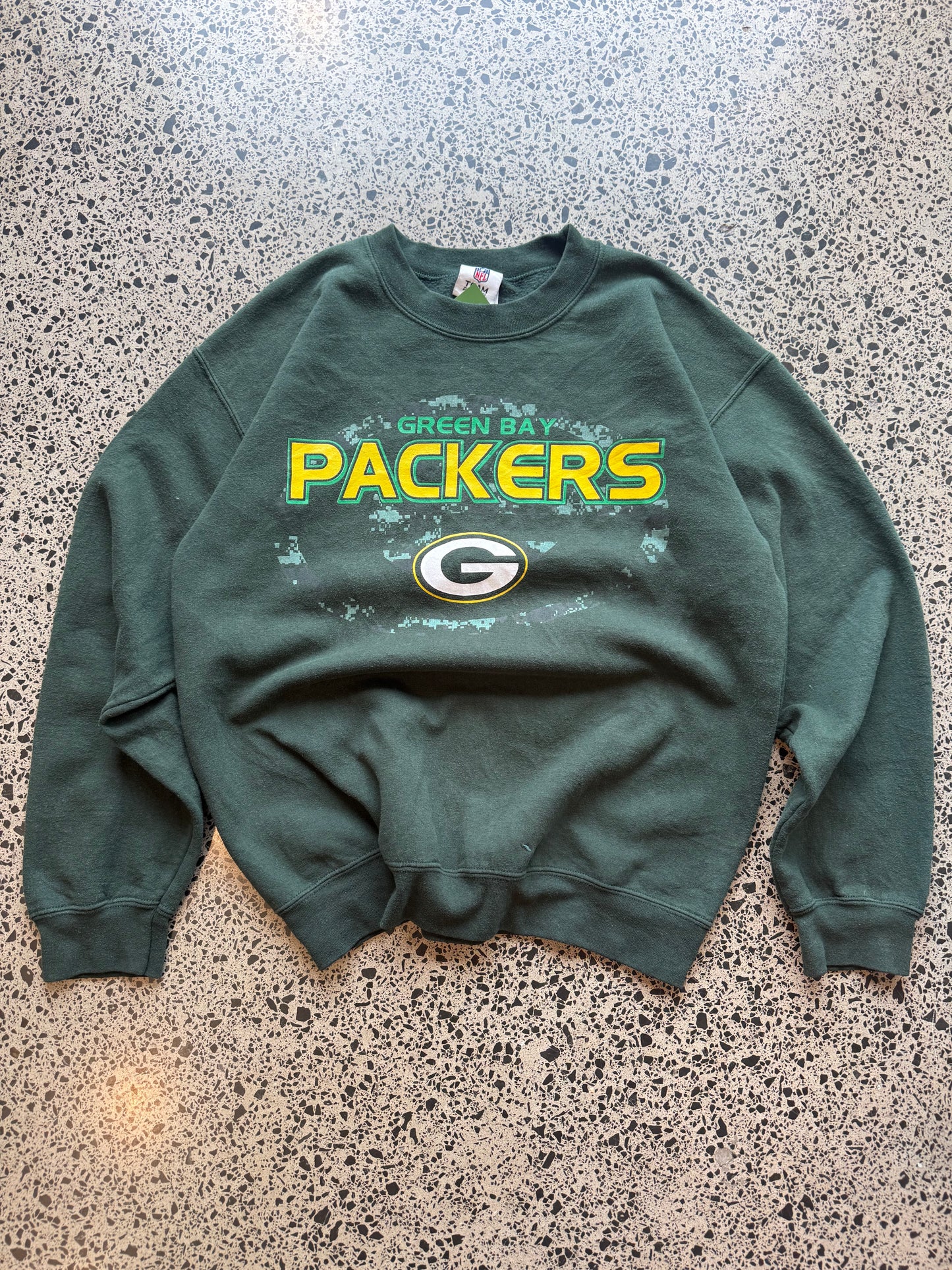 90s Green Bay Packers NFL crewneck jumper size medium laid flat on polished concrete background, vintage football sweatshirt with bold team graphics and classic fit