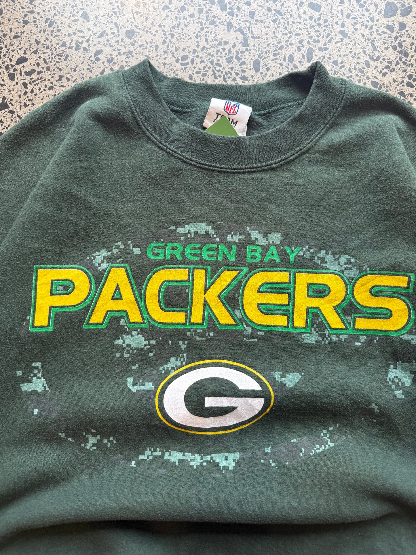 90s Green Bay Packers NFL crewneck jumper size medium laid flat on polished concrete background, vintage football sweatshirt with bold team graphics and classic fit