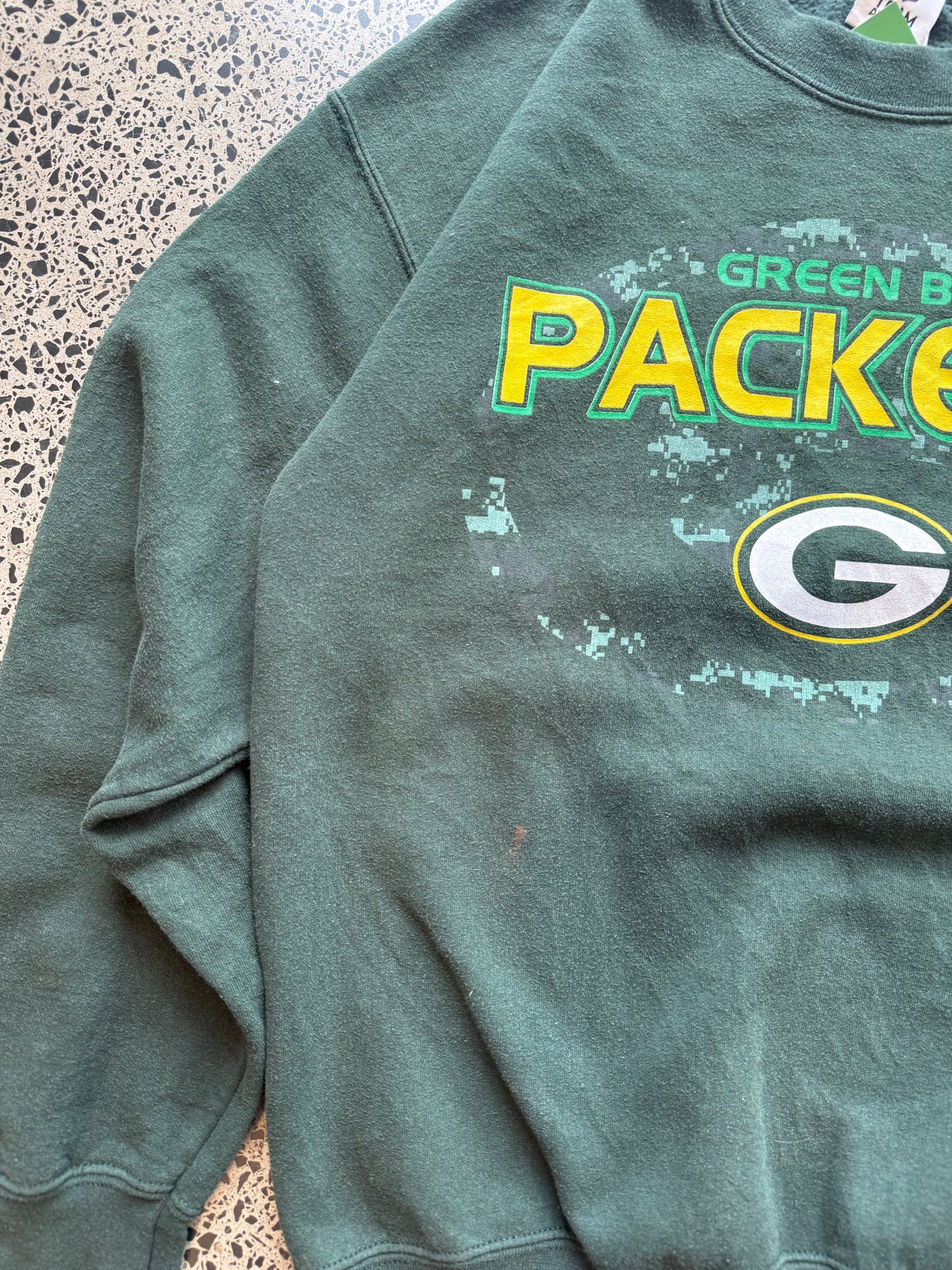 90s Green Bay Packers NFL crewneck jumper size medium laid flat on polished concrete background, vintage football sweatshirt with bold team graphics and classic fit