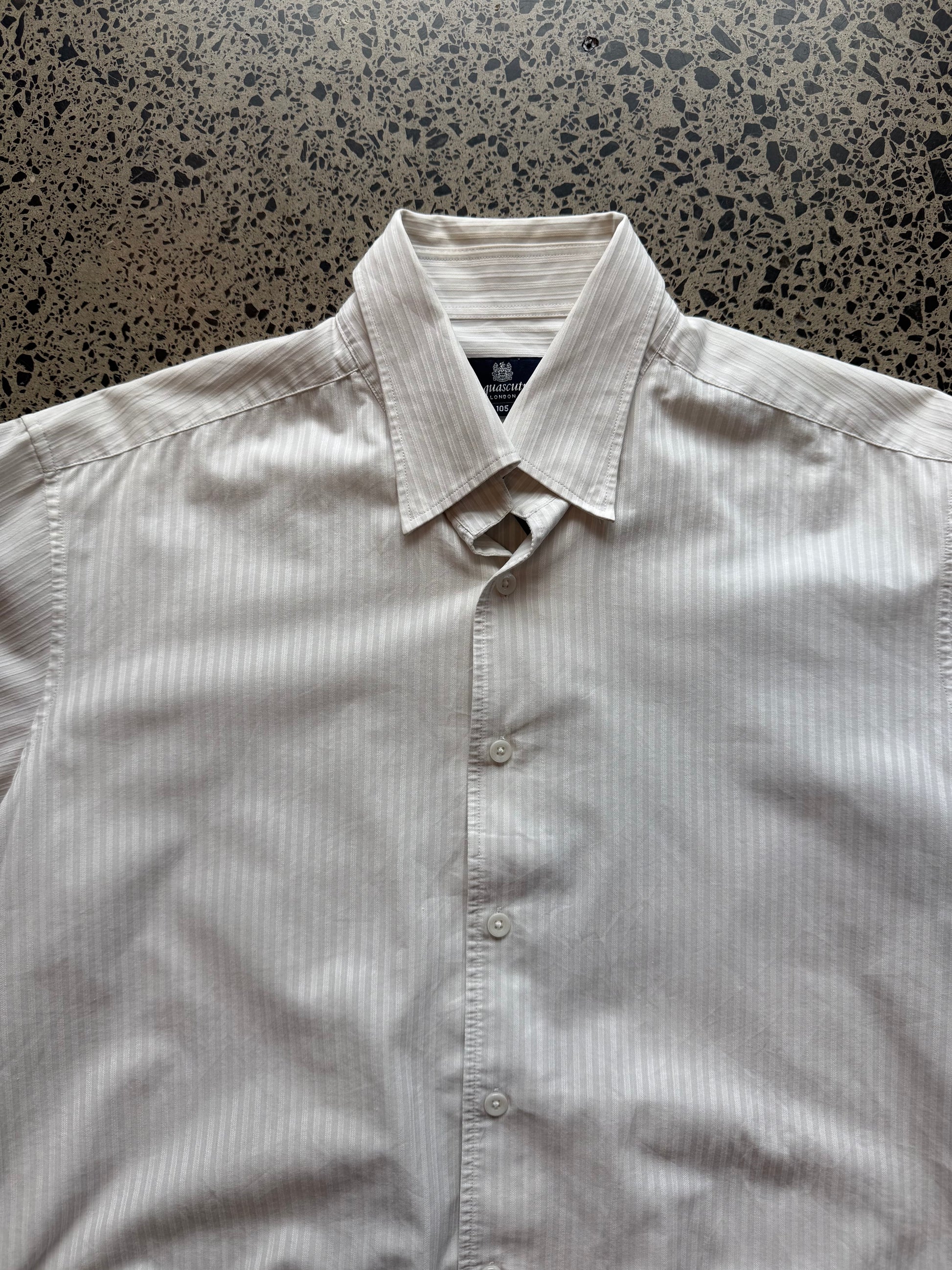 Aquascutum button-up shirt in size L laid flat on a polished concrete background featuring clean British heritage tailoring.