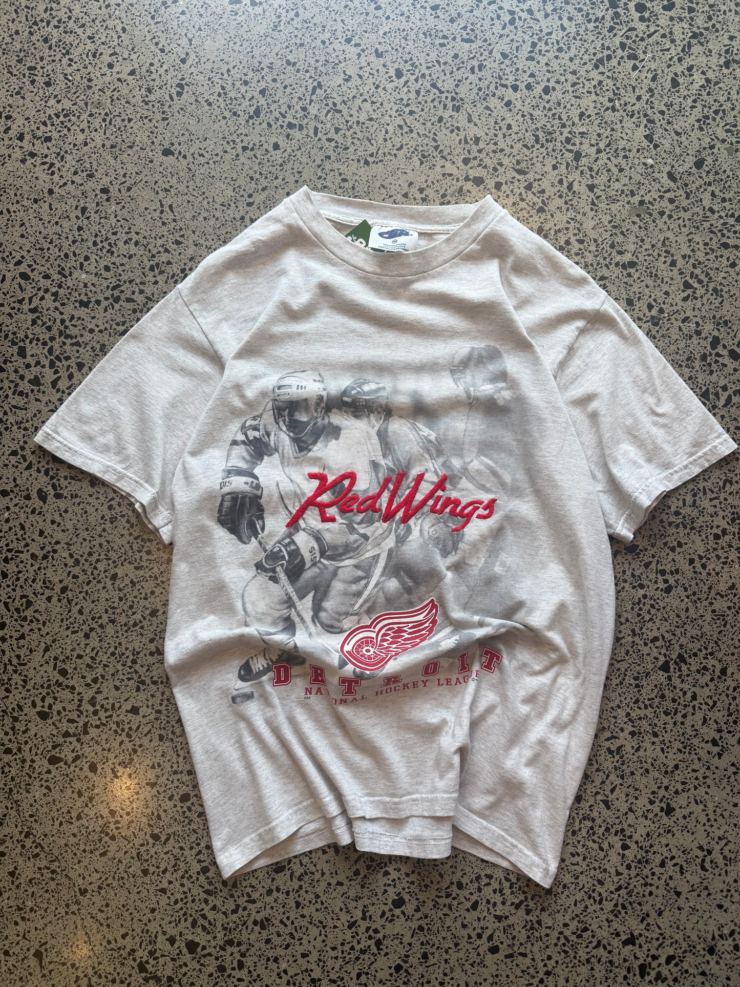 90s Detroit Red Wings NHL T-shirt, red, size M, laid on polished concrete background — vintage hockey graphic on soft cotton.