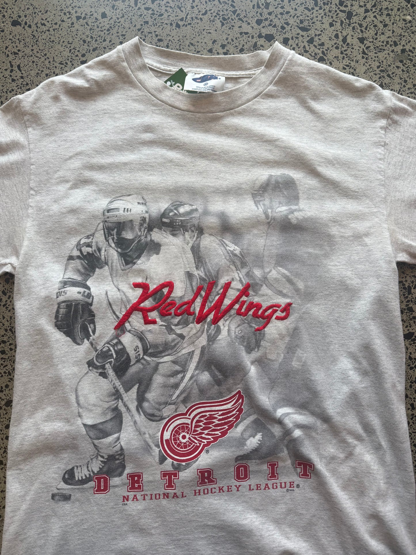 90s Detroit Red Wings NHL T-shirt, red, size M, laid on polished concrete background — vintage hockey graphic on soft cotton.