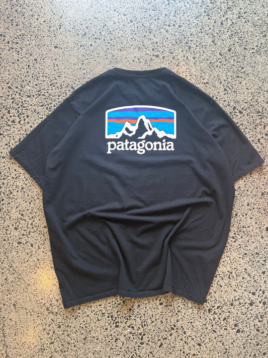 Patagonia mountain graphic T-shirt, size L, laid on polished concrete background — outdoor-inspired print on soft cotton.