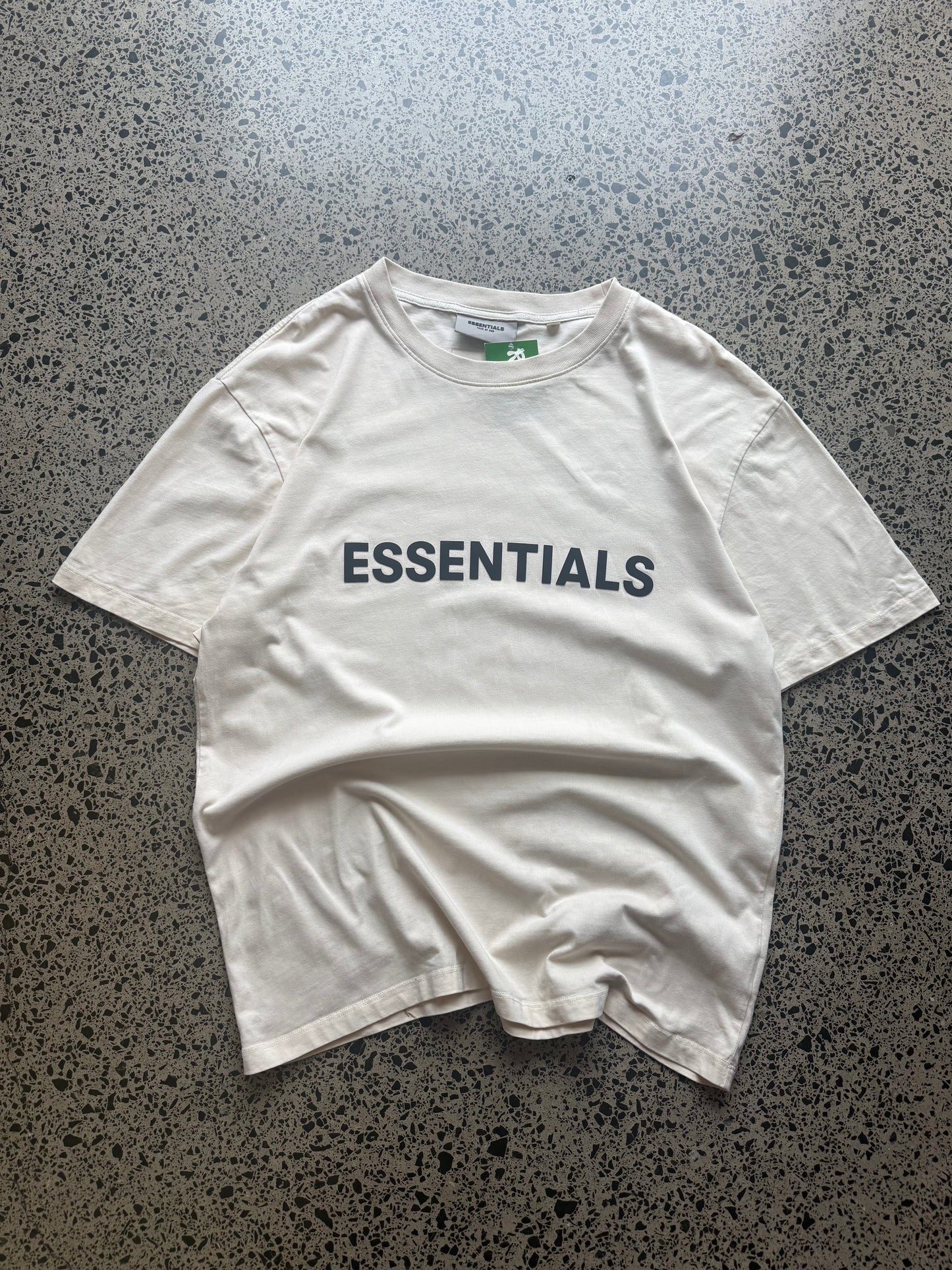 Fear of God Essentials t-shirt size M laid flat on polished concrete background, minimal streetwear tee with subtle Essentials branding and relaxed fit.