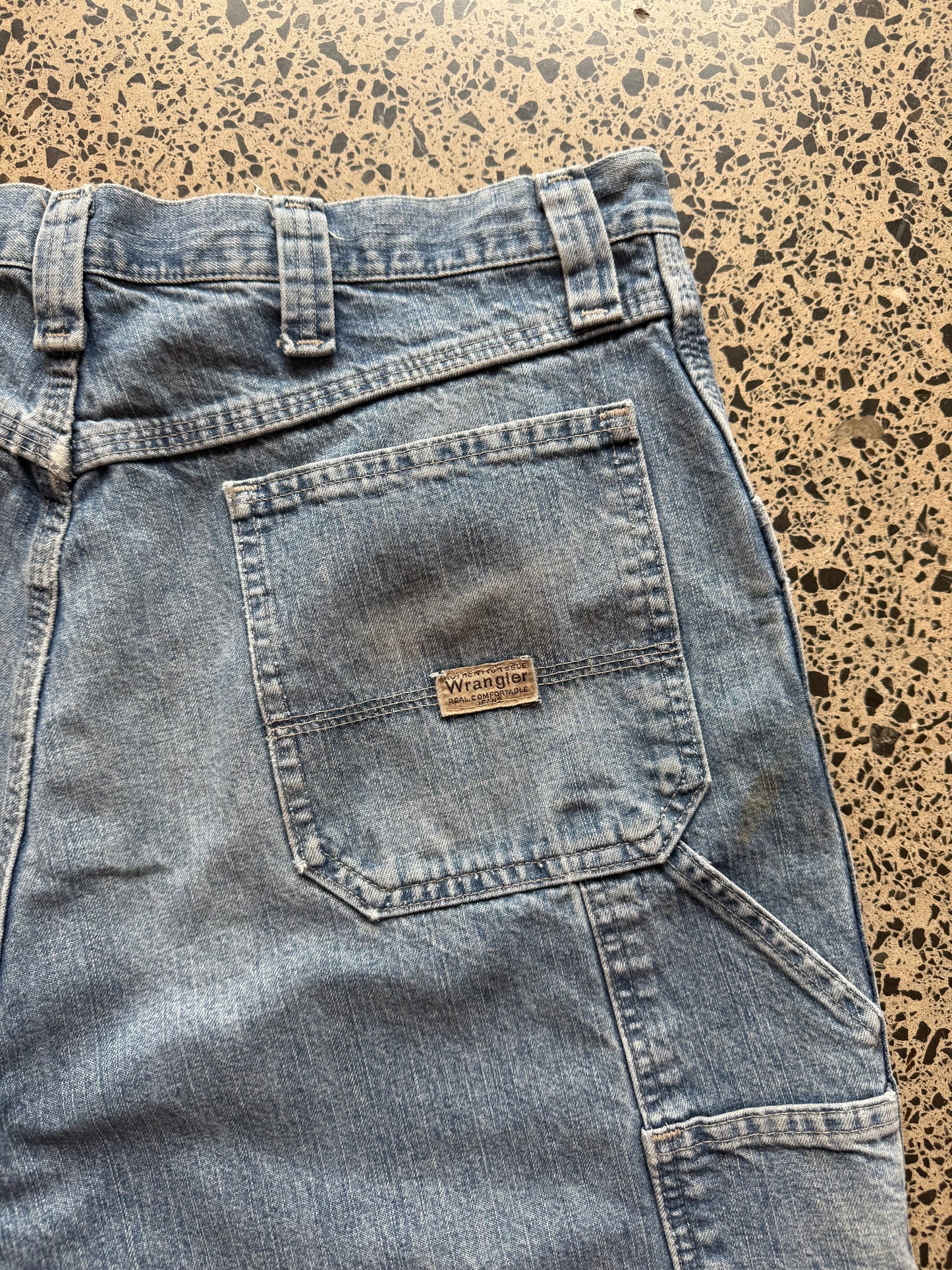 Wrangler Original light blue wash denim jorts, size 34W, laid on polished concrete background. Knee cut with classic stitching and soft wash