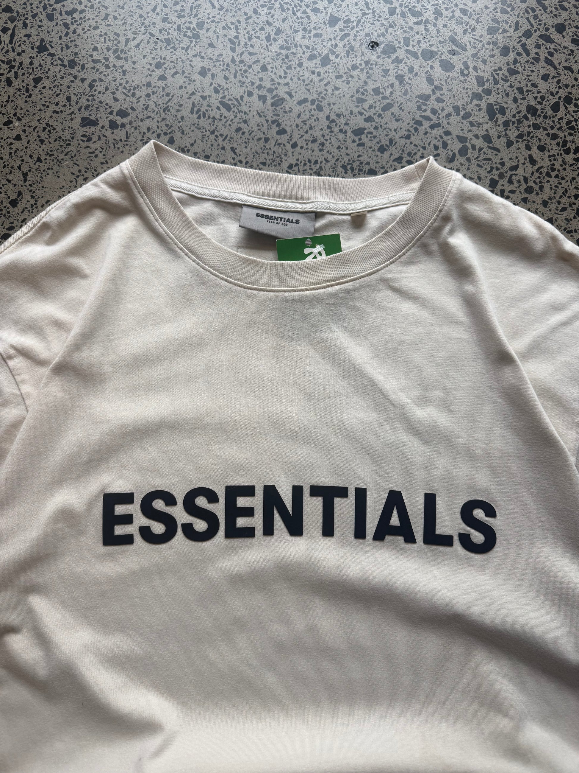 Fear of God Essentials t-shirt size M laid flat on polished concrete background, minimal streetwear tee with subtle Essentials branding and relaxed fit.