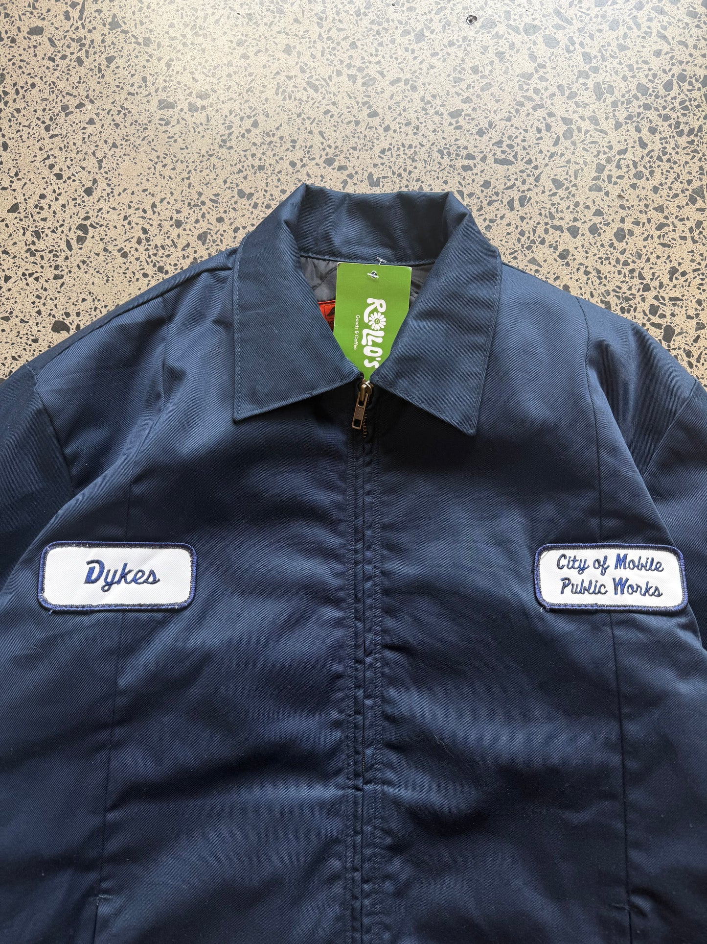 Red Kap workwear zipper jacket size Small Regular laid on polished concrete background — dark navy with zip front and pockets.