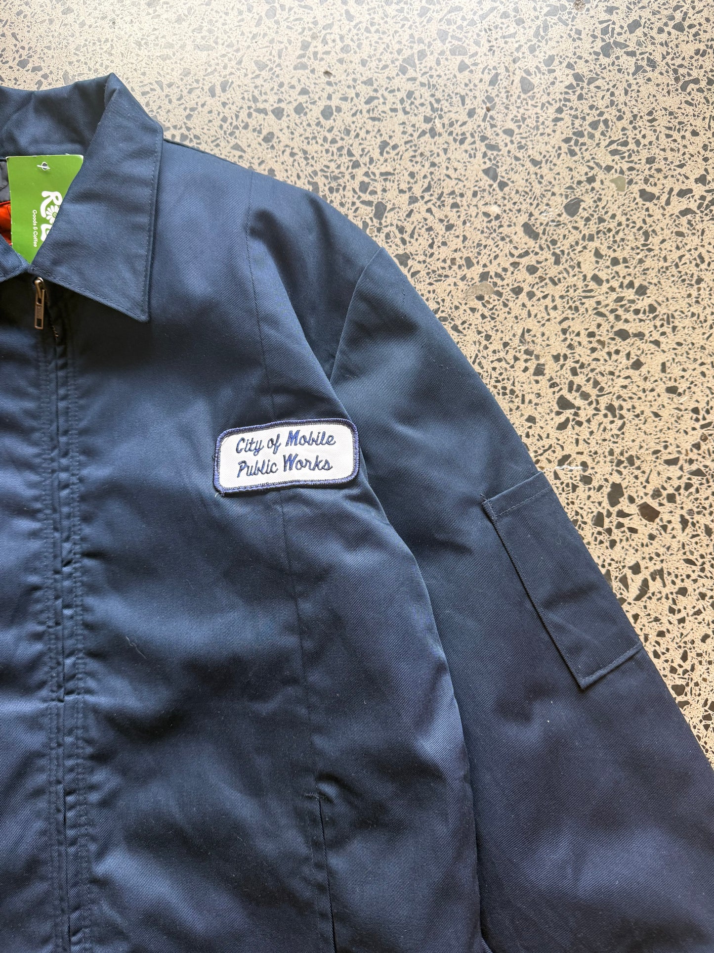Red Kap workwear zipper jacket size Small Regular laid on polished concrete background — dark navy with zip front and pockets.
