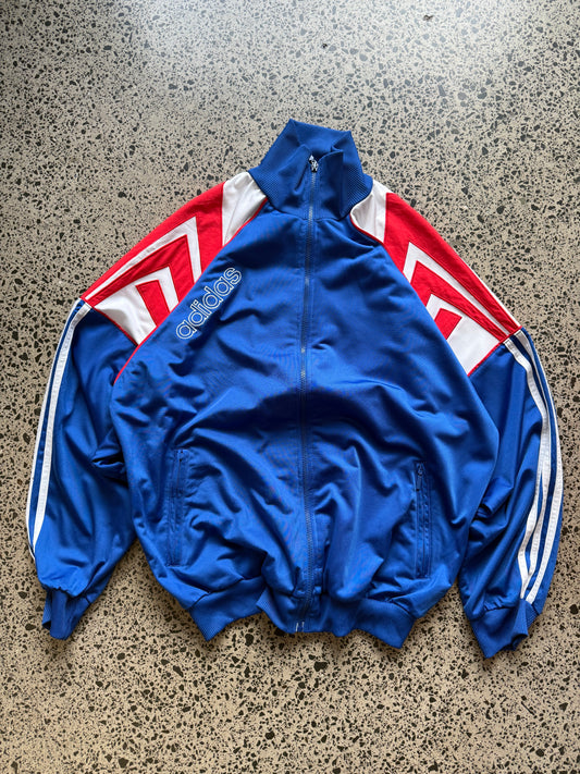 90s vintage Adidas zip-up track jacket size L laid on polished concrete background — black with white 3-stripe detailing and Adidas logo.