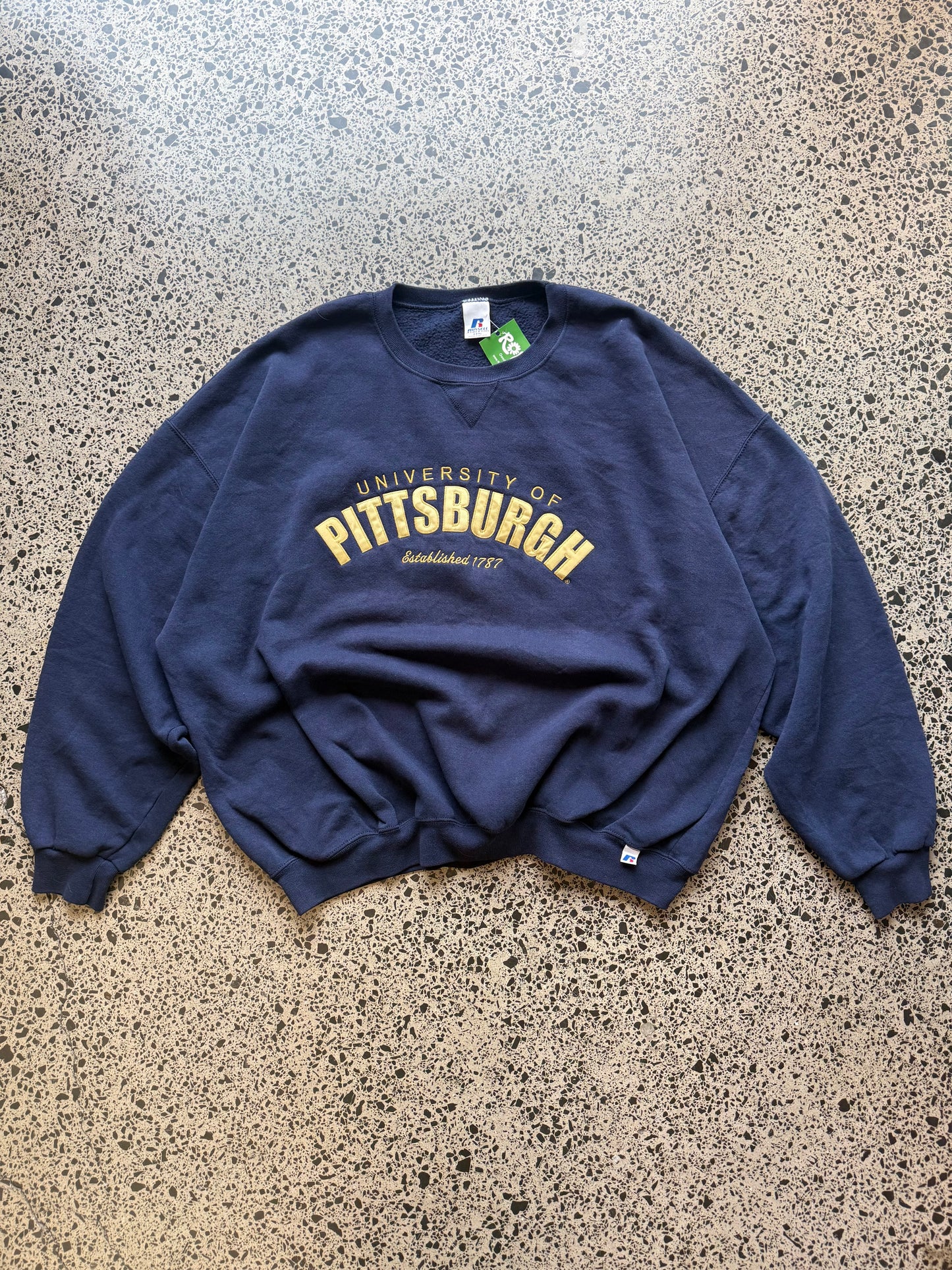 90s University of Pittsburgh crewneck jumper size 3XL laid flat on polished concrete background, vintage college sweatshirt with bold lettering and oversized fit.