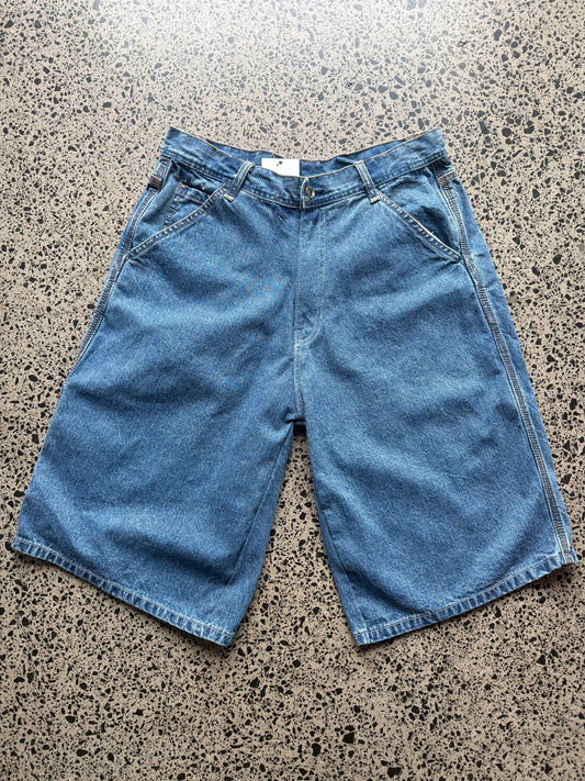 Arizona mid wash denim jorts, size 30W, laid on polished concrete background — below knee cut t with classic stitching and soft faded wash.