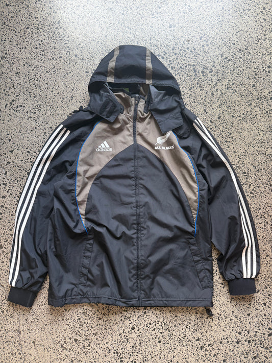2000s All Blacks rugby jacket size XL laid on polished concrete background — black with silver detailing and All Blacks logo.