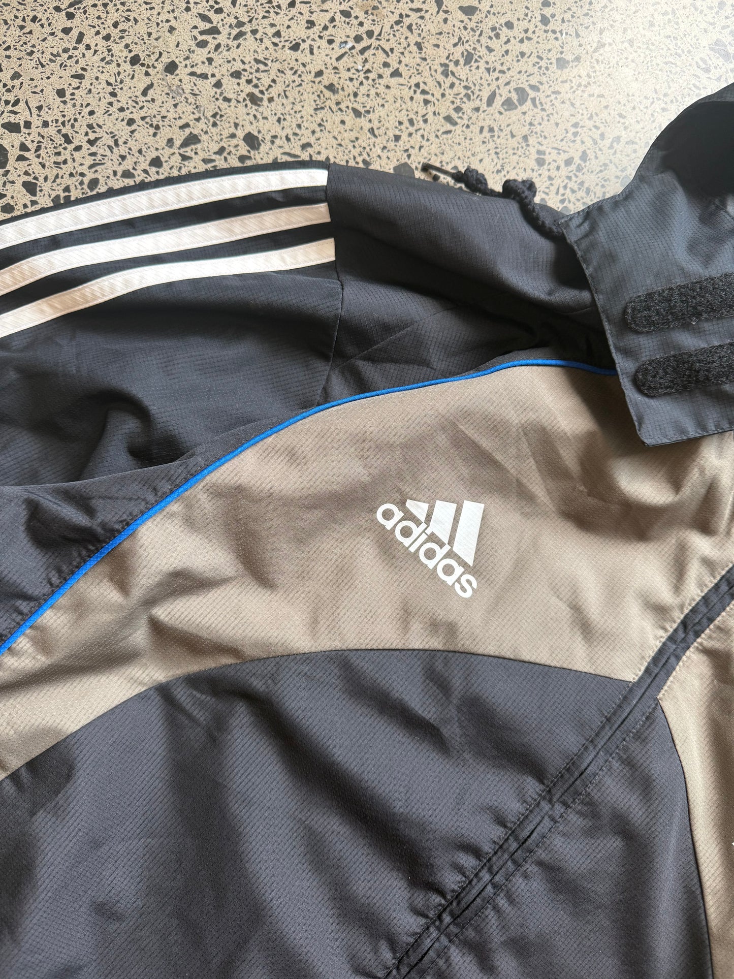 2000s All Blacks rugby jacket size XL laid on polished concrete background — black with silver detailing and All Blacks logo.