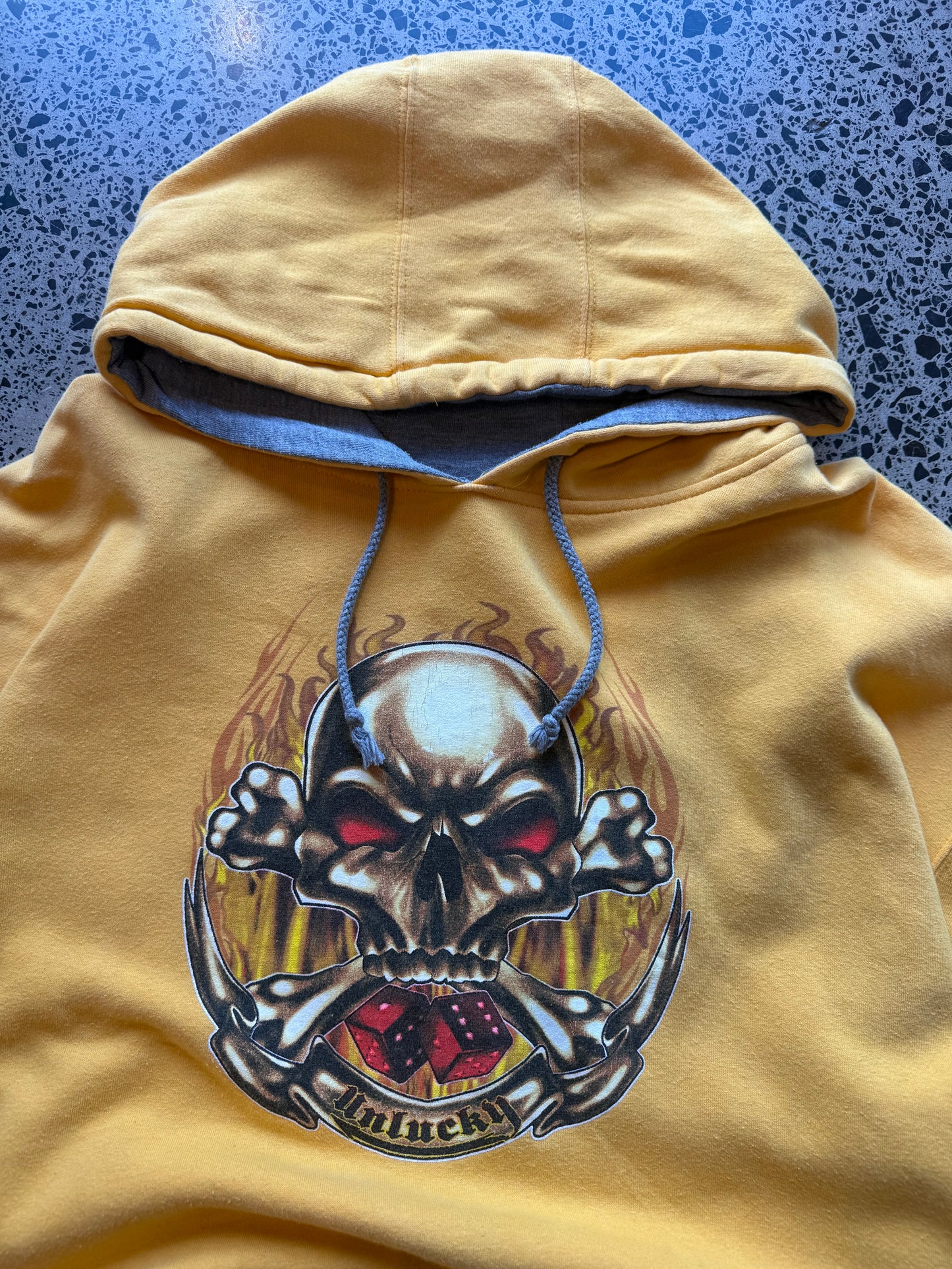 Y2K Top Heavy skull and bones hoodie XL laid flat on polished concrete background, vintage streetwear hoodie with bold graphic print and relaxed fit.