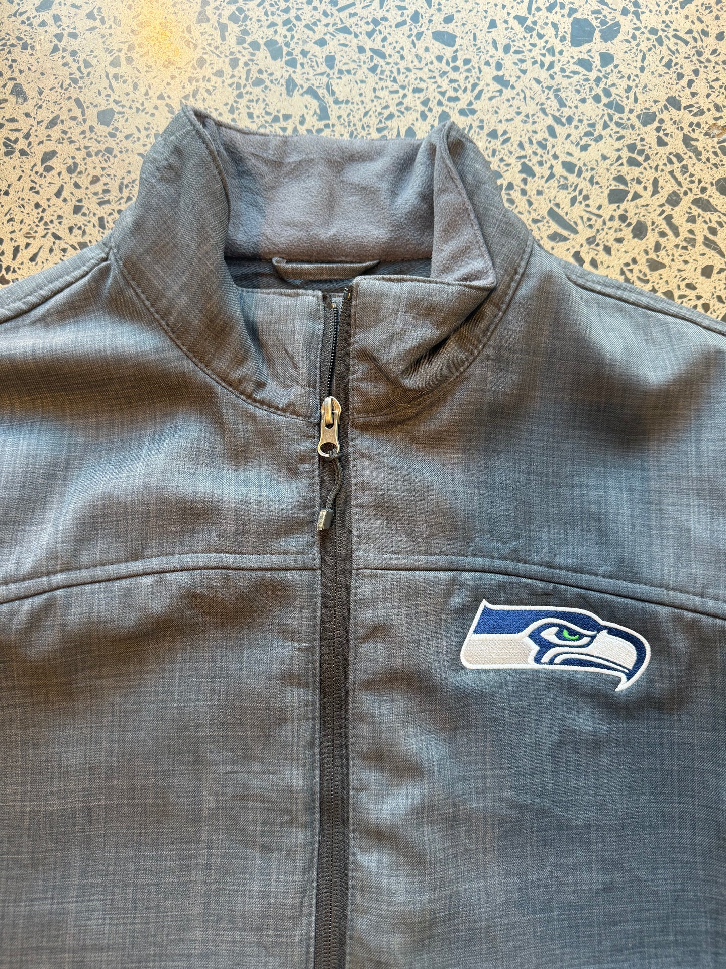 Seattle Seahawks NFL soft shell jacket size M laid flat on polished concrete background, lightweight sportswear jacket with subtle team branding and clean fit.