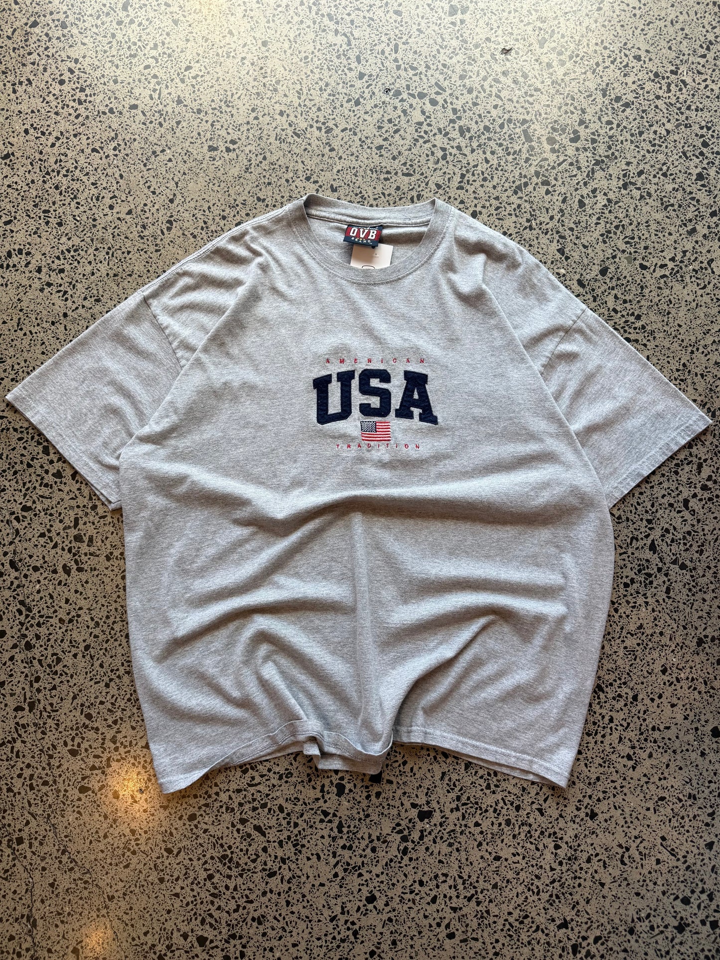 USA flag graphic T-shirt in size 2XL laid on a polished concrete background with vintage-style print.