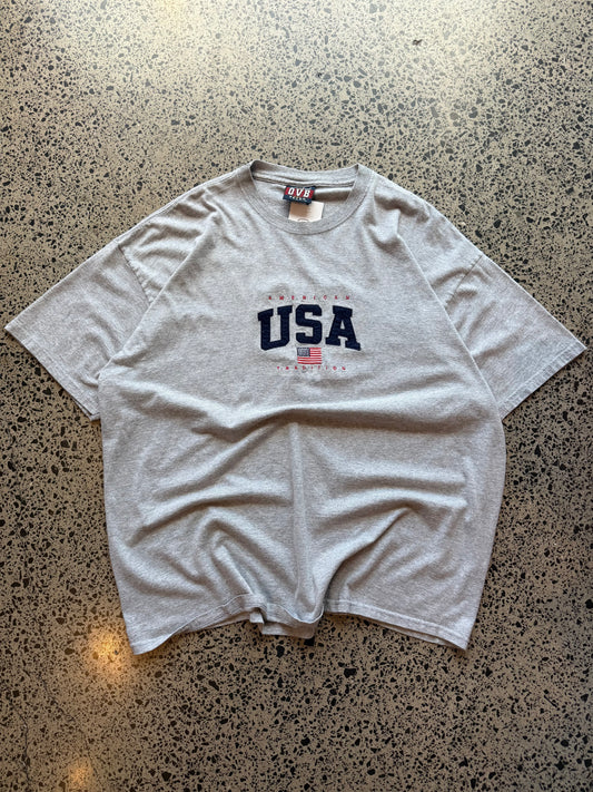 USA flag graphic T-shirt in size 2XL laid on a polished concrete background with vintage-style print.