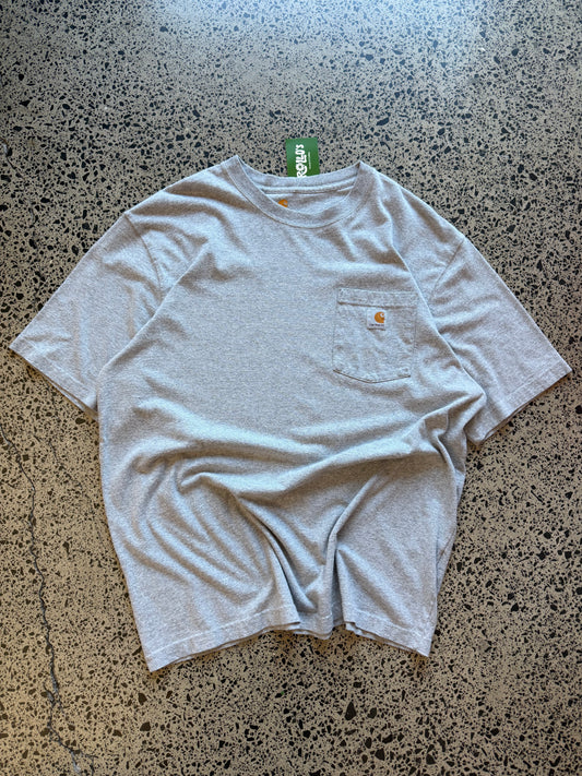 Grey Carhartt pocket t-shirt with chest logo patch, size L, laid flat on a polished concrete background