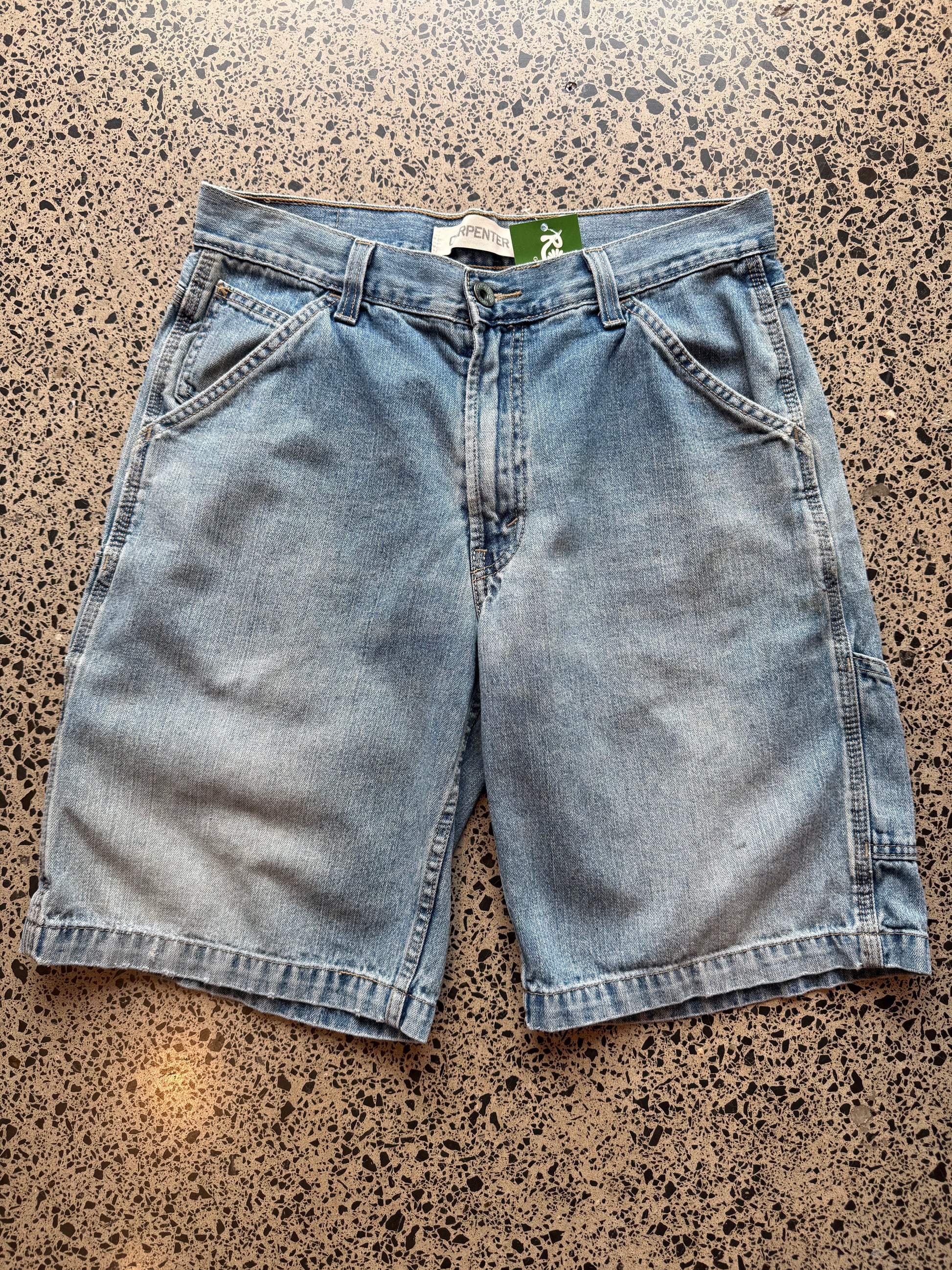 Levi's light blue wash denim jorts, size 32W, laid on polished concrete background. Knee cut with classic stitching and soft wash