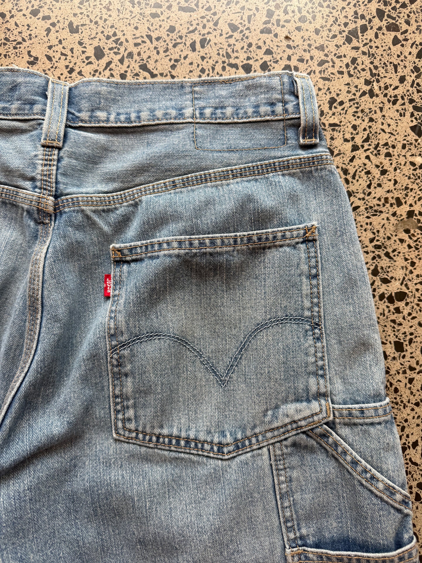 Levi's light blue wash denim jorts, size 32W, laid on polished concrete background. Knee cut with classic stitching and soft wash