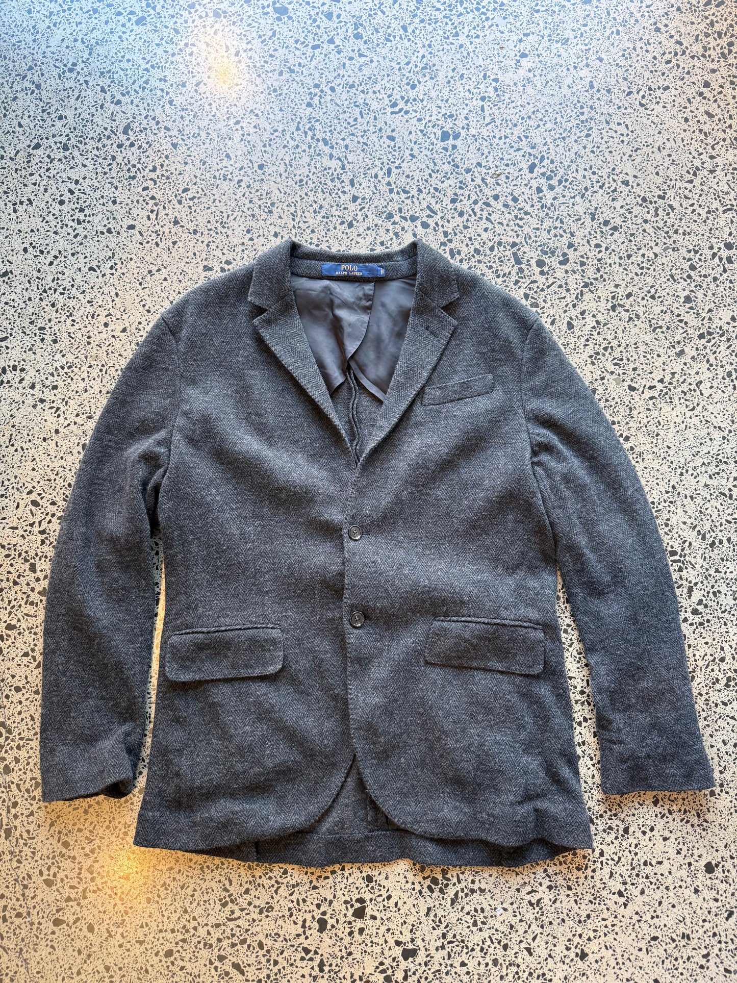 Ralph Lauren herringbone 100 percent wool blazer jacket laid flat on polished concrete background, classic tailored jacket with textured pattern and clean fit.