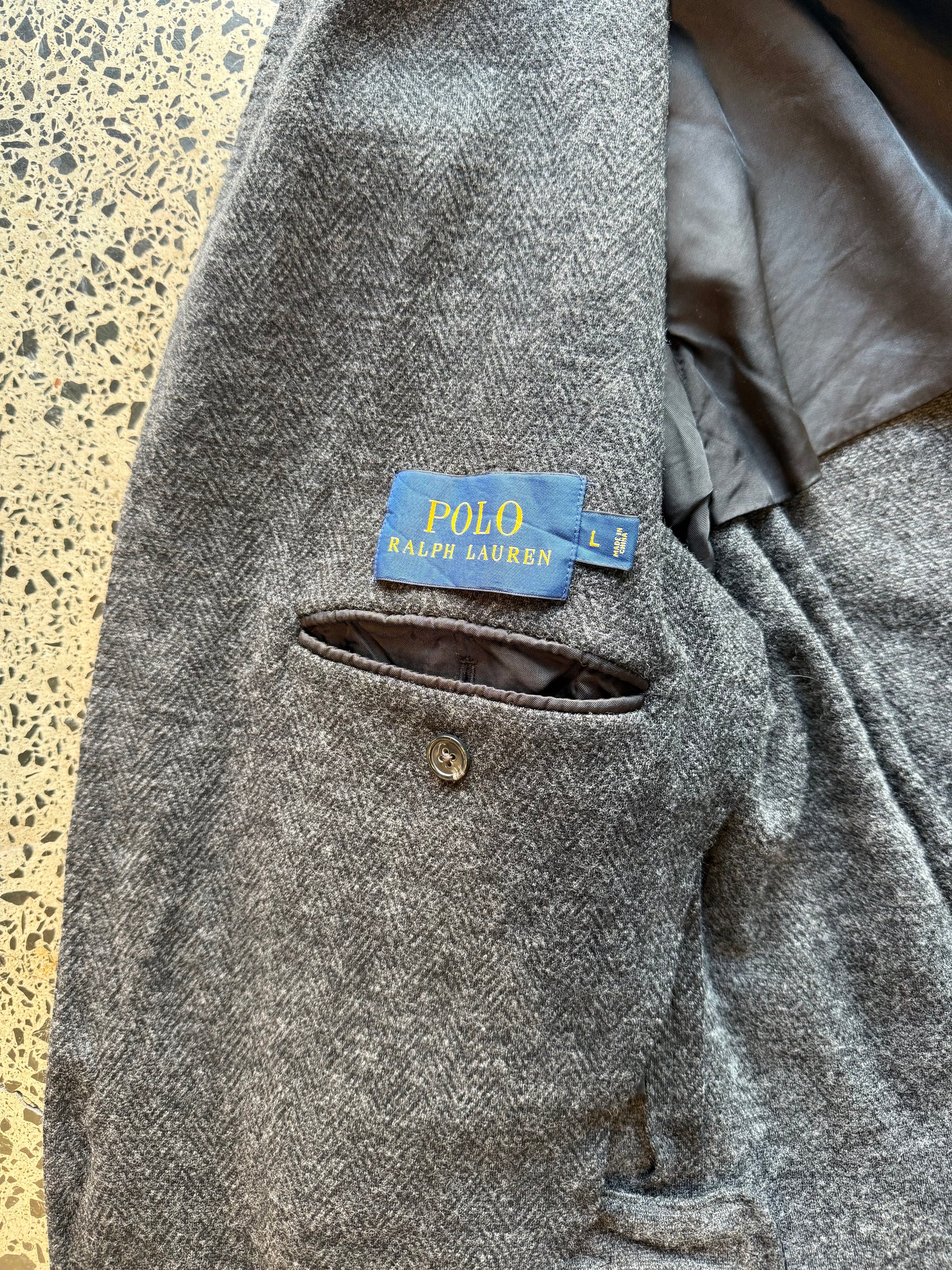 Ralph Lauren herringbone 100 percent wool blazer jacket laid flat on polished concrete background, classic tailored jacket with textured pattern and clean fit.
