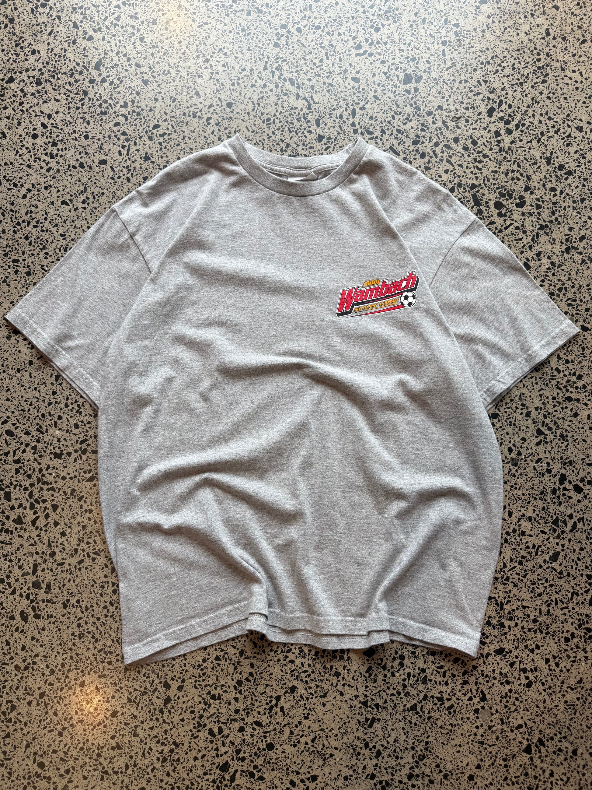 2000s Nike Abby Wambach Soccer Camp T-shirt in size M laid on a polished concrete background featuring U.S. women’s soccer camp graphic.