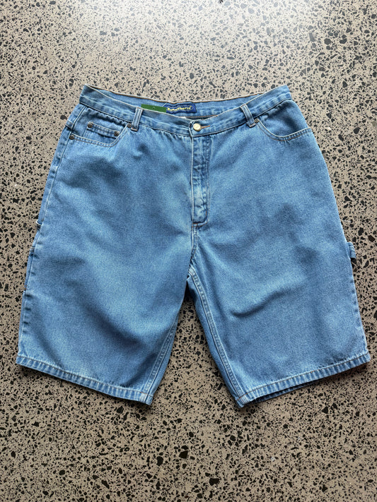 Kneeshorts  light-wash denim jorts, size 30W, laid on polished concrete background. Just above knee cut with classic stitching and soft wash
