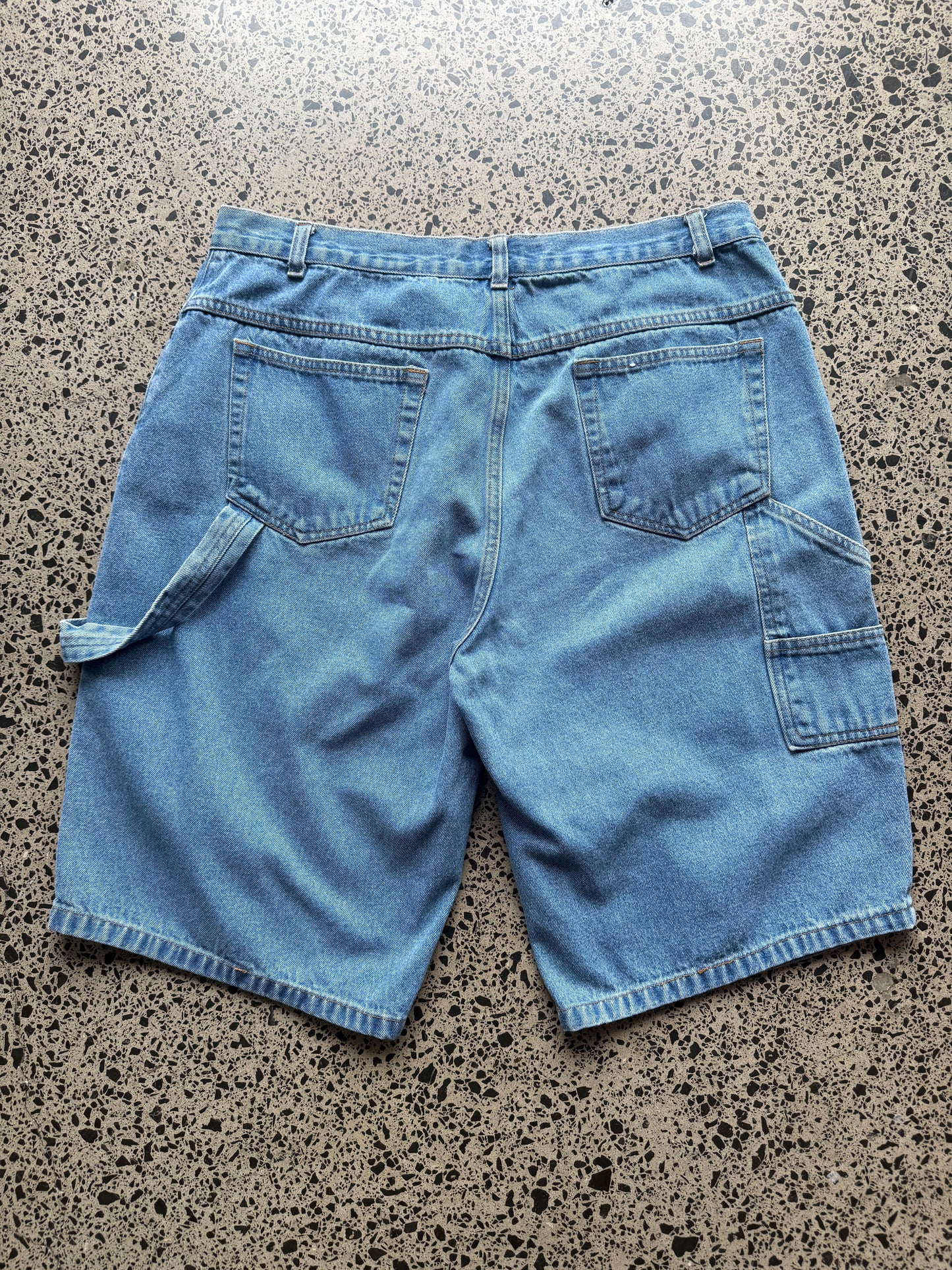 Kneeshorts  light-wash denim jorts, size 30W, laid on polished concrete background. Just above knee cut with classic stitching and soft wash