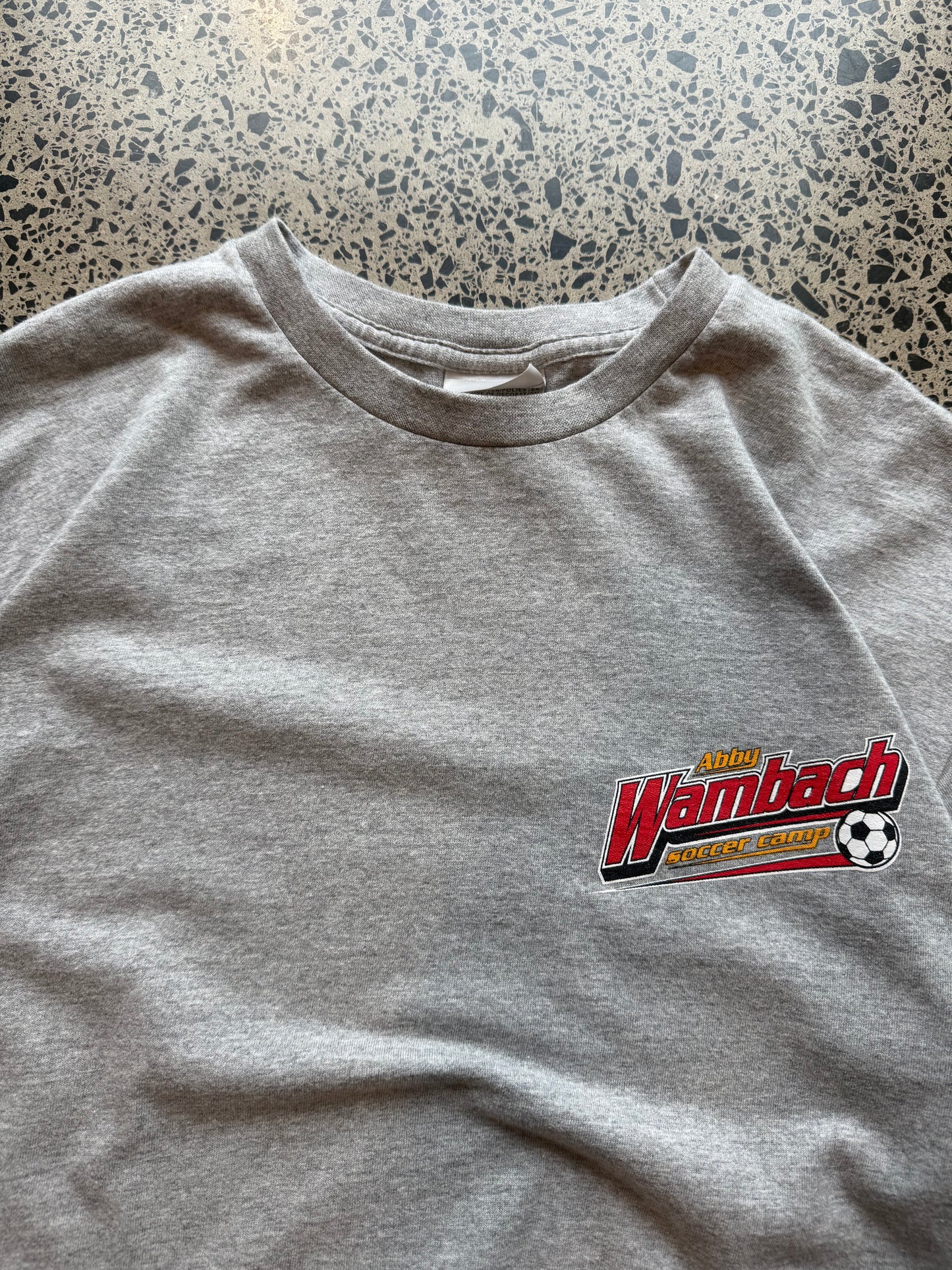 2000s Nike Abby Wambach Soccer Camp T-shirt in size M laid on a polished concrete background featuring U.S. women’s soccer camp graphic.
