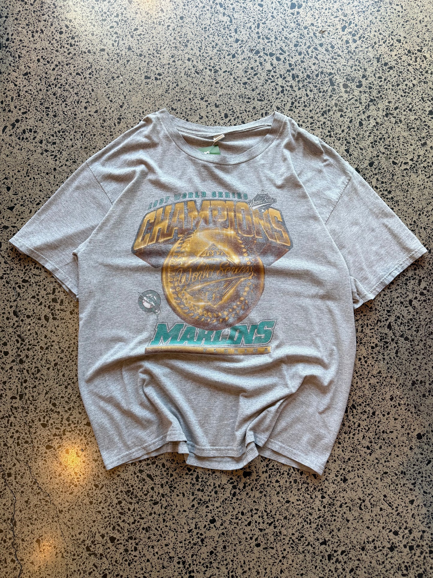 1997 Miami Marlins World Series Champions graphic T-shirt, size 2XL, laid on polished concrete background — bold vintage MLB championship print on soft cotton.
