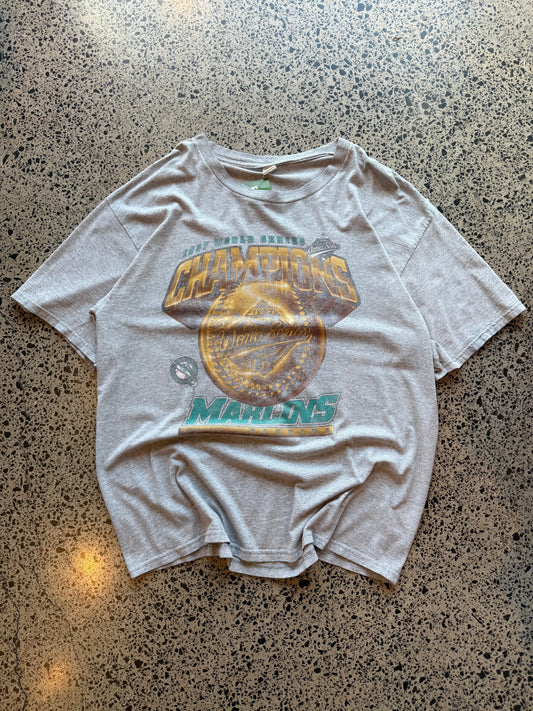 1997 Miami Marlins World Series Champions graphic T-shirt, size 2XL, laid on polished concrete background — bold vintage MLB championship print on soft cotton.