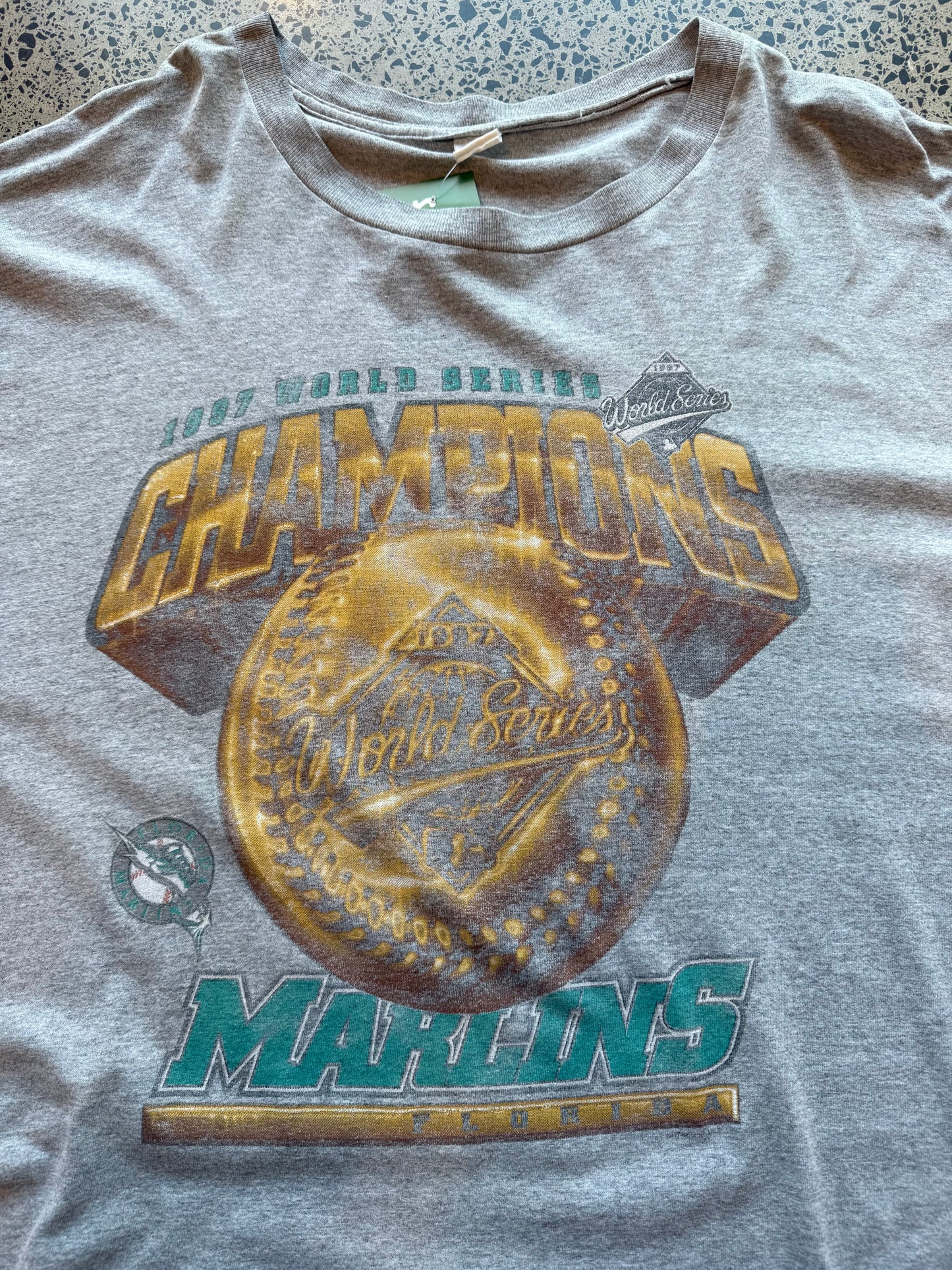 1997 Miami Marlins World Series Champions graphic T-shirt, size 2XL, laid on polished concrete background — bold vintage MLB championship print on soft cotton.