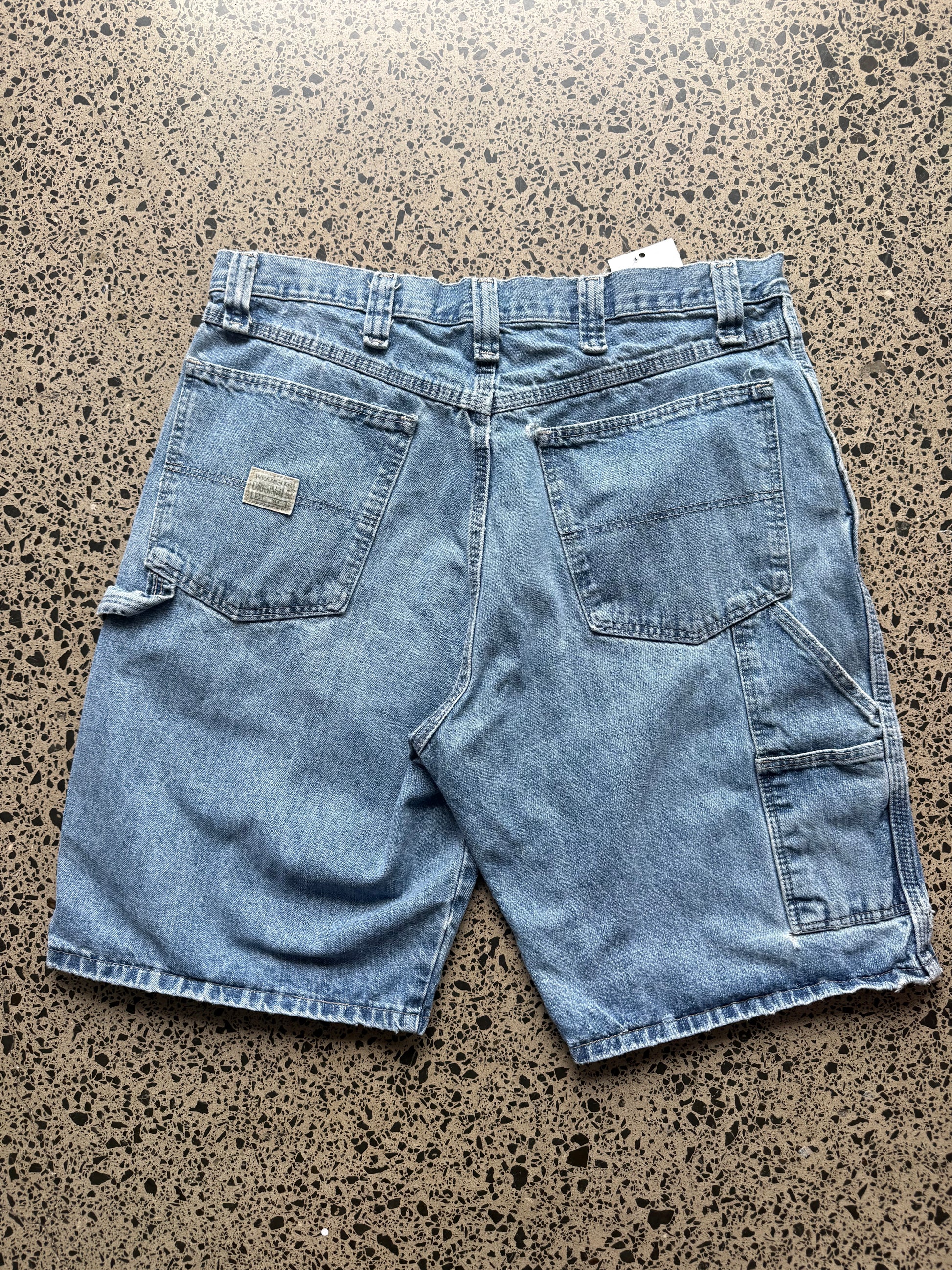 Wrangler original  light-wash denim jorts, size 34W, laid on polished concrete background. Knee cut with classic stitching and soft wash