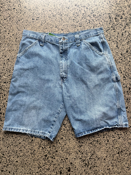 Wrangler original  light-wash denim jorts, size 34W, laid on polished concrete background. Knee cut with classic stitching and soft wash