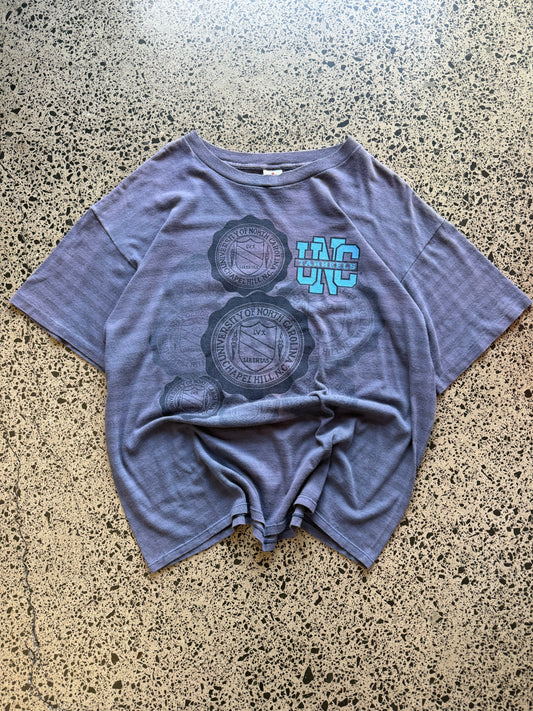 Faded blue 80s North Carolina Tarheels graphic t-shirt with a chest print, size XL, laid flat on a polished concrete background