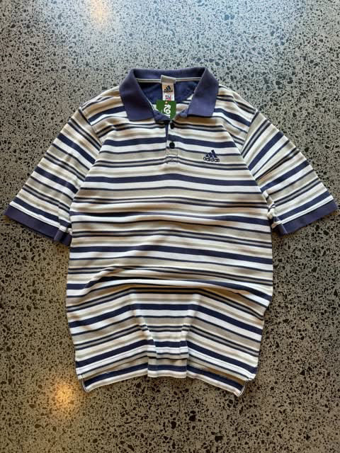 Vintage striped Adidas collared shirt laid flat on polished concrete background with classic stripe pattern and embroidered Adidas Trefoil logo.