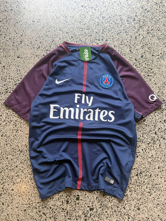 2017/18 Paris Saint-Germain home football jersey in size M laid on a polished concrete background. navy PSG kit with red and white centre stripe
