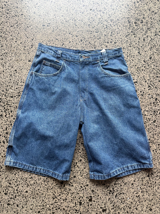 Wrangler Original dark blue wash denim jorts, size 32W, laid on polished concrete background. Knee cut with classic stitching and soft wash