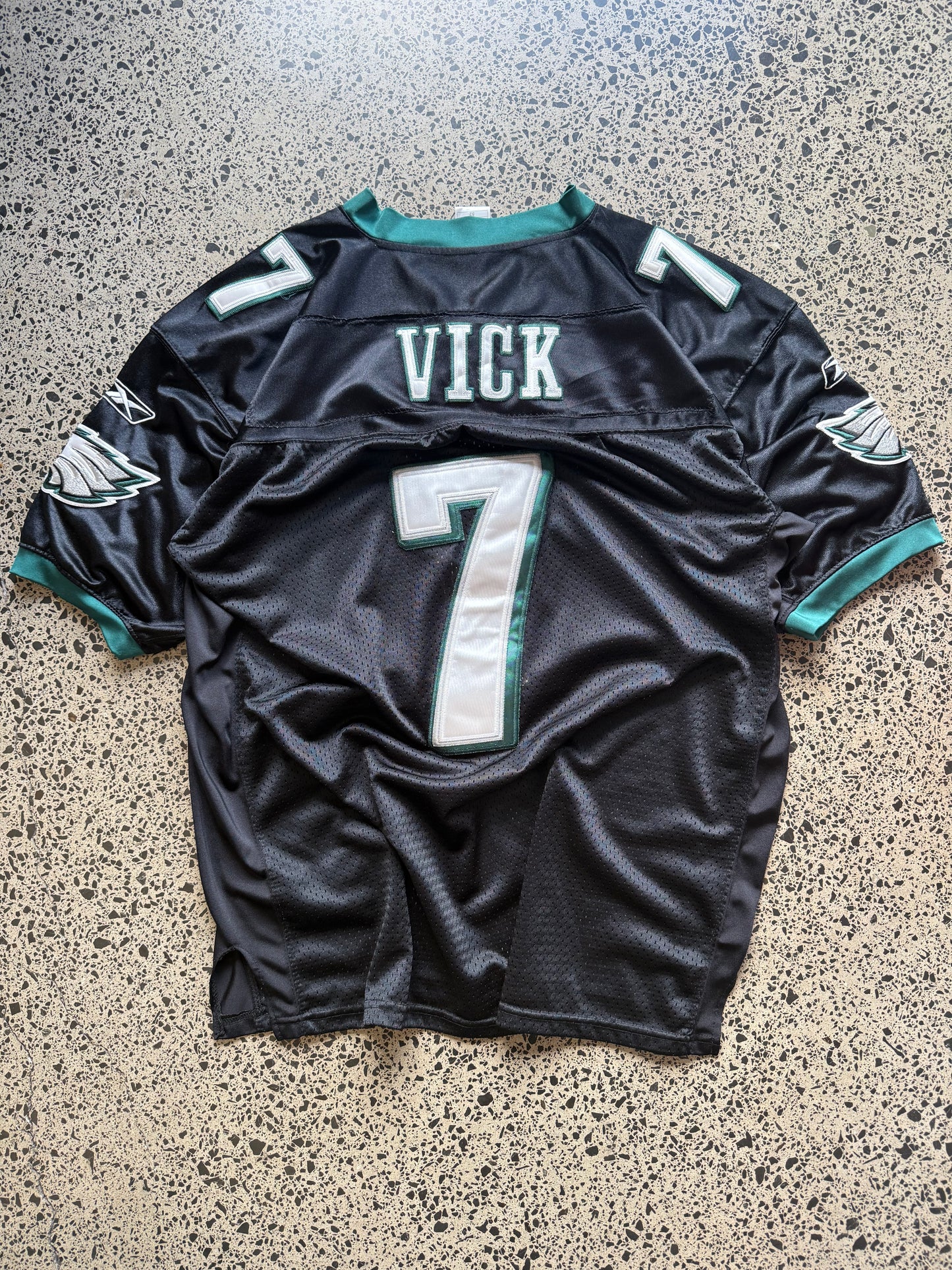 Philadelphia Eagles Michael Vick NFL jersey size 2XL laid on polished concrete background — midnight green with white detailing and Eagles logo.