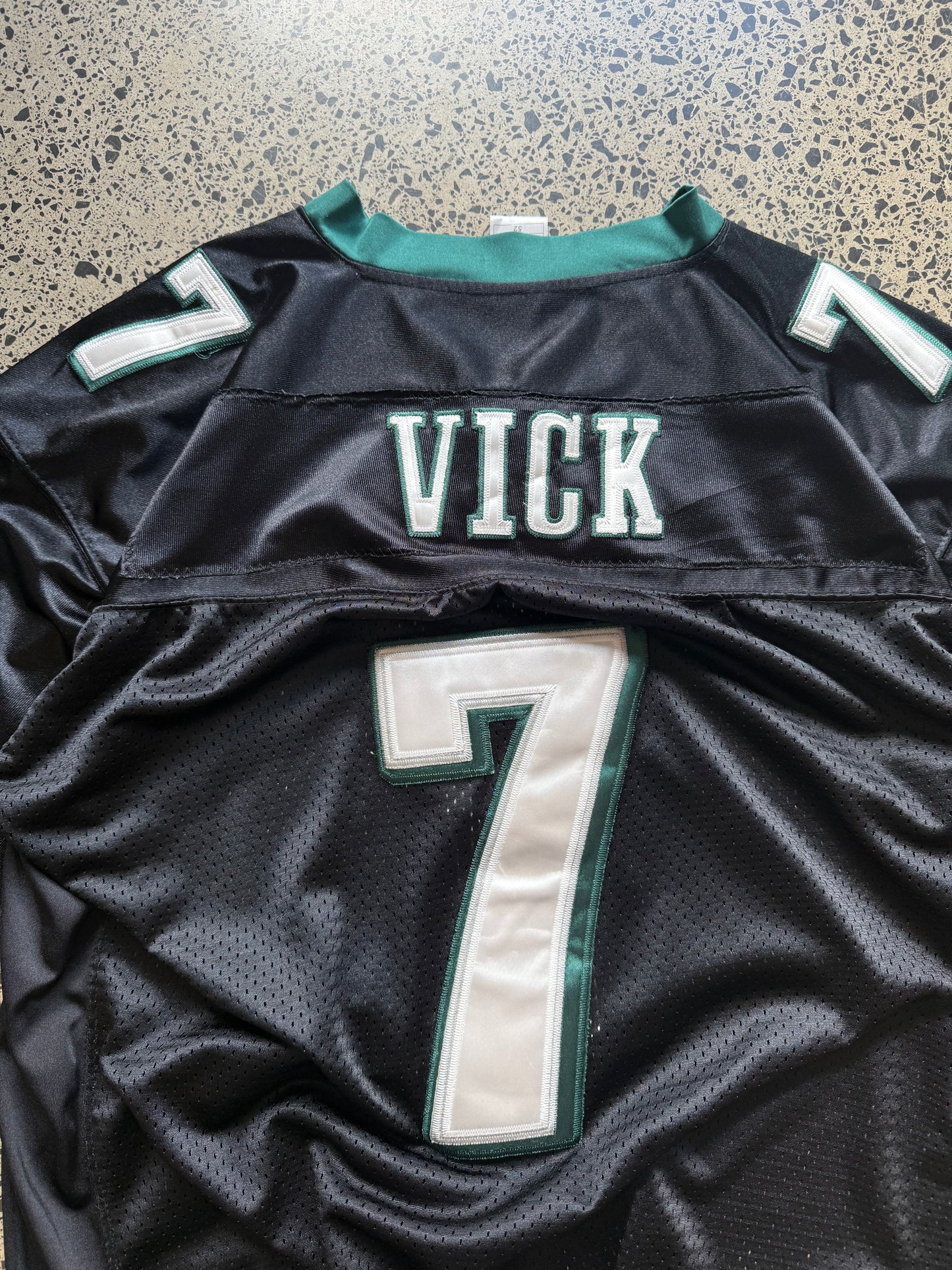 Philadelphia Eagles Michael Vick NFL jersey size 2XL laid on polished concrete background — midnight green with white detailing and Eagles logo.