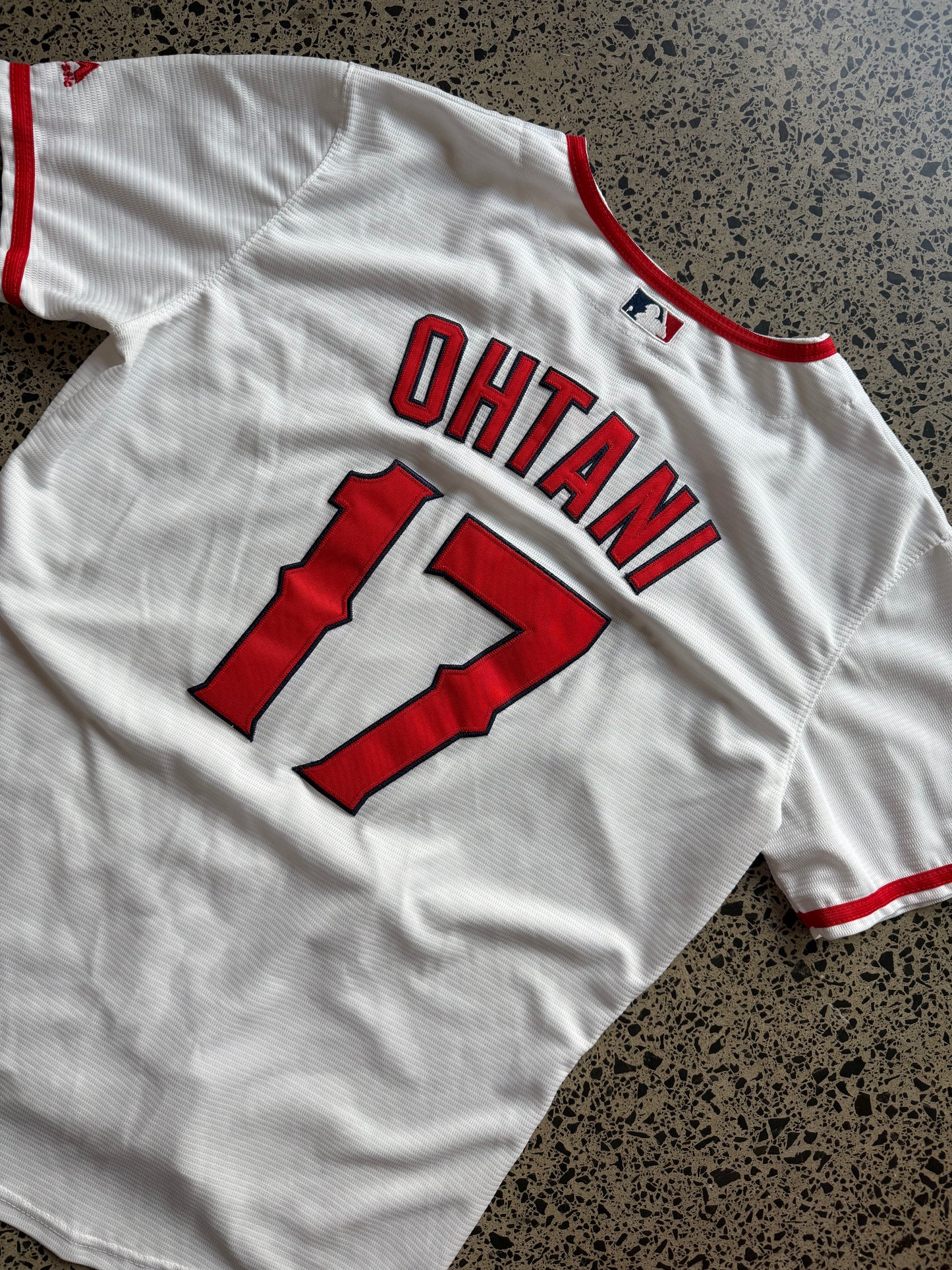 LA Angels Shohei Ohtani MLB baseball jersey size XL laid on polished concrete background — red with white detailing and Angels logo.