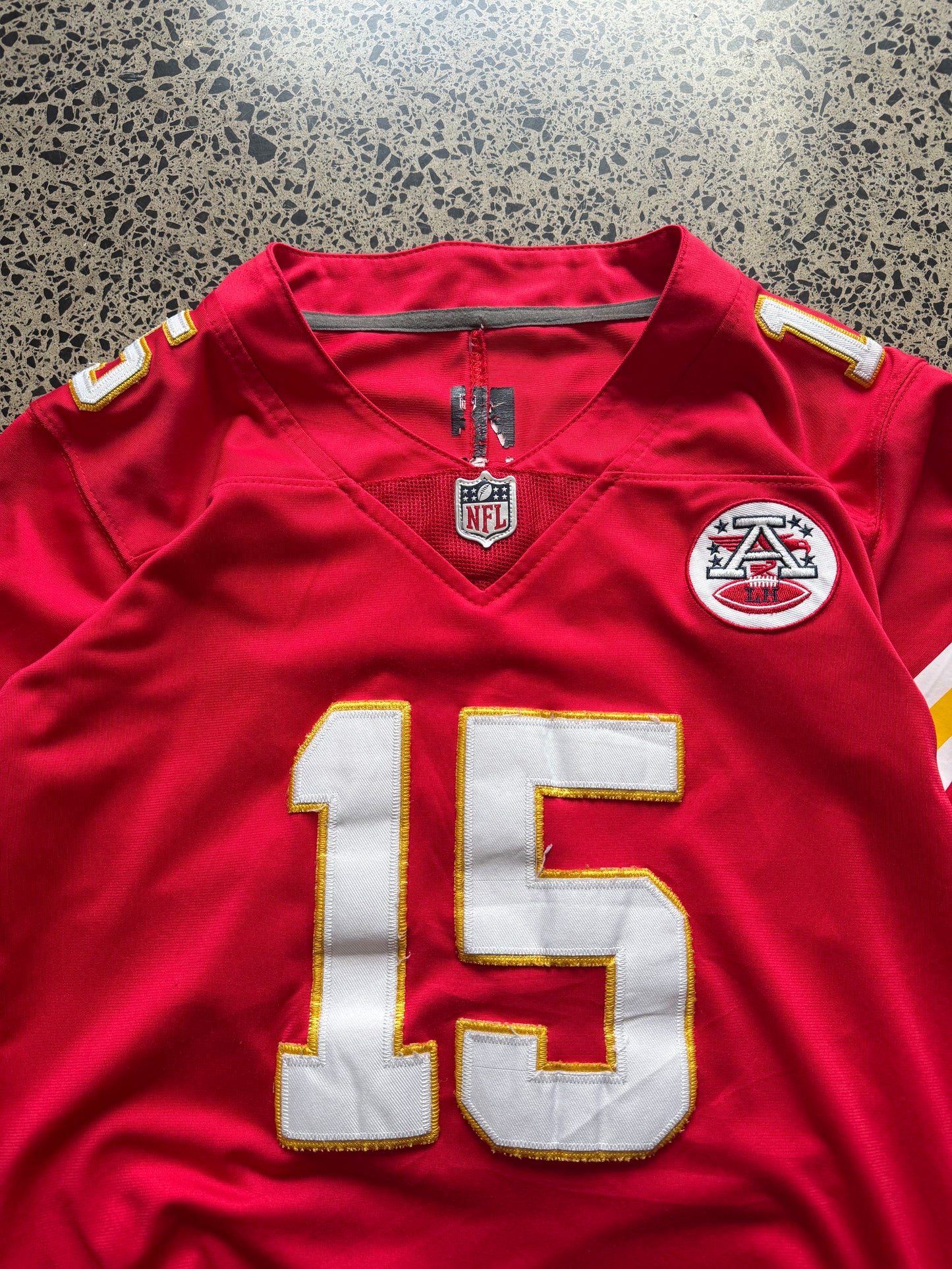Kansas City Chiefs Patrick Mahomes NFL jersey in Youth Large laid on polished concrete background — red with white and yellow detailing and Chiefs logo.