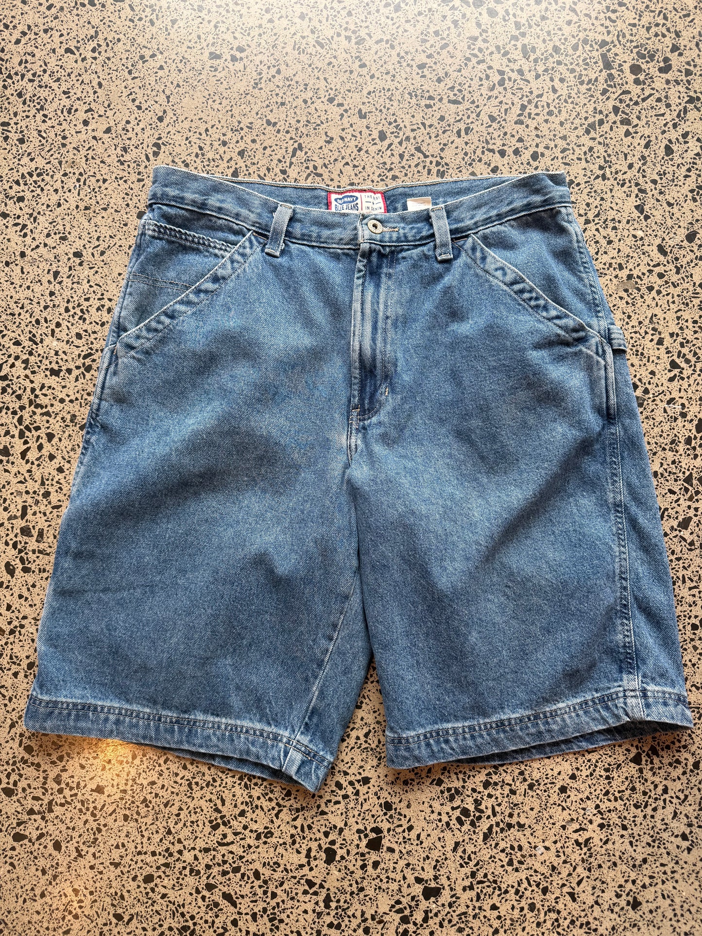 Old Navy dark blue wash denim jorts, size 34W, laid on polished concrete background. Knee cut with classic stitching and soft wash
